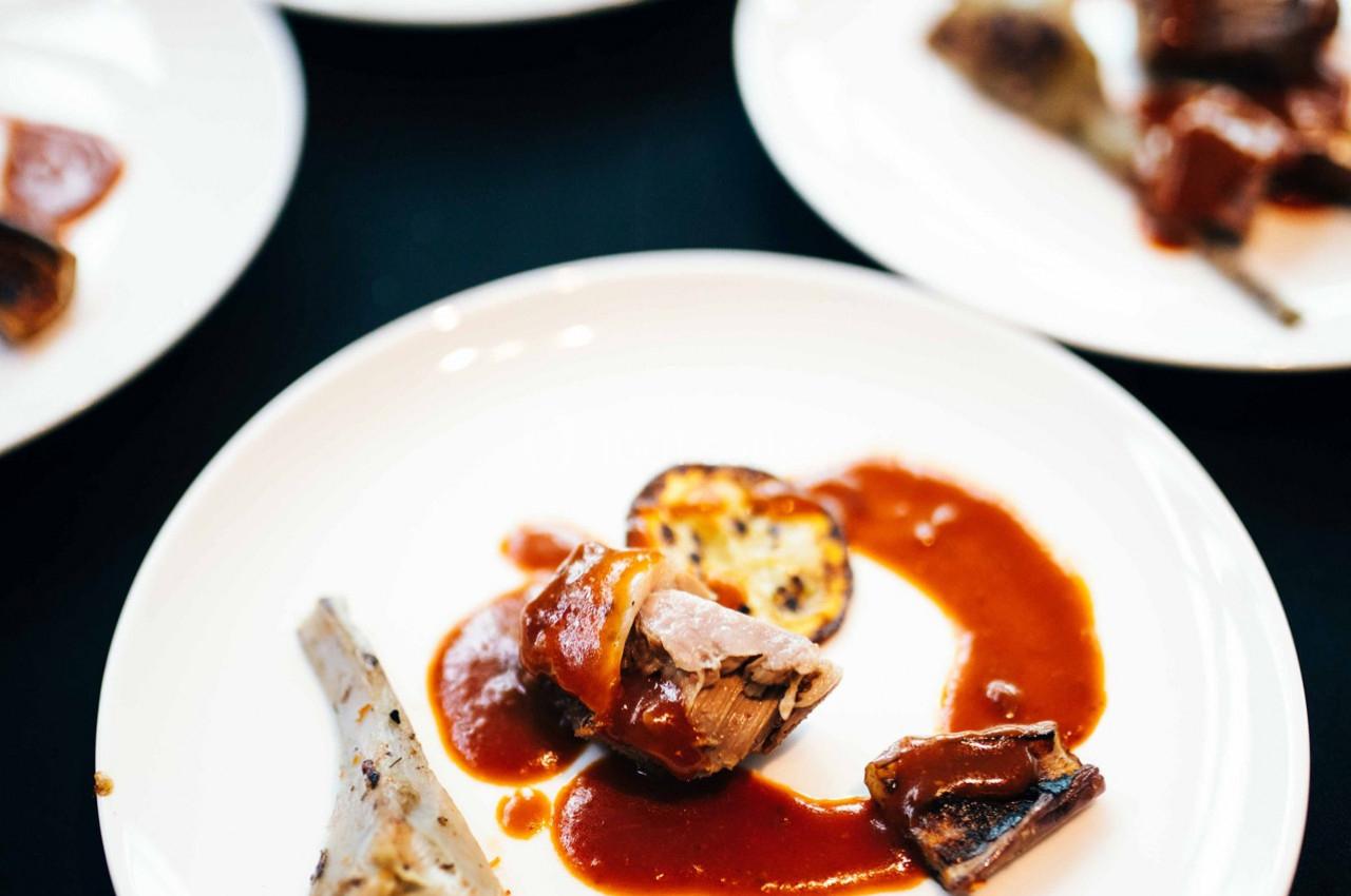 Assiette contenant un plat gastronomique avec viande, sauce rouge et accompagnements disposés de manière soignée.