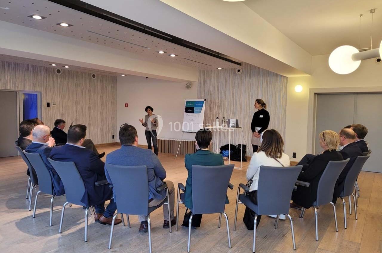 Une personne présente un exposé à un groupe assis en cercle dans une salle lumineuse et moderne.