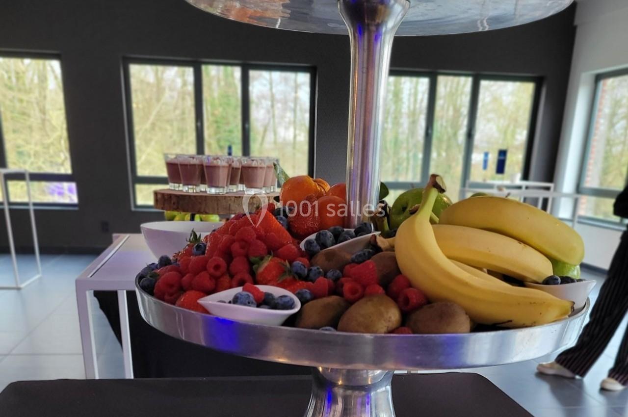Plateau de fruits variés avec bananes, kiwis, baies et oranges, posé dans une salle lumineuse avec vue sur l'extérieur.