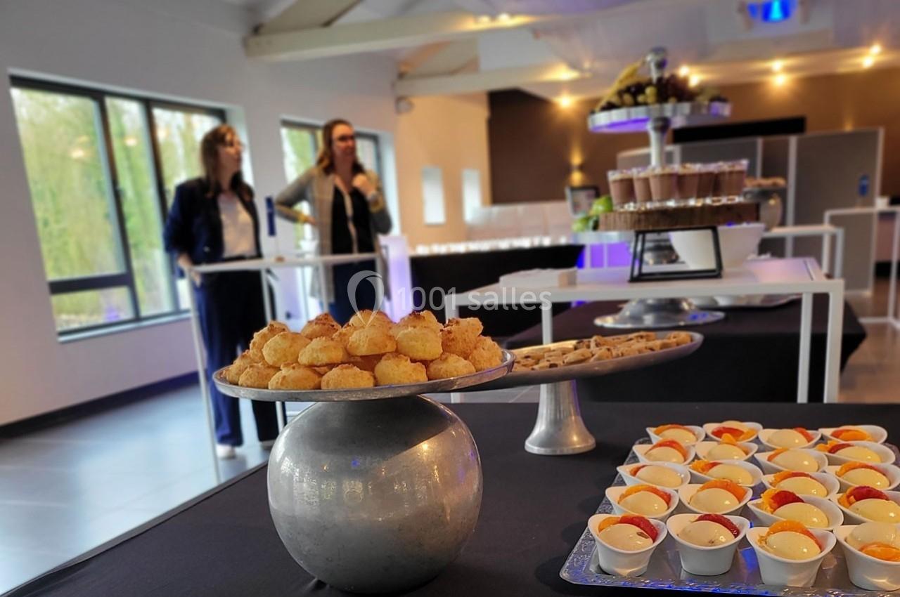 Plateau de desserts variés sur une table dans une salle lumineuse avec deux personnes en arrière-plan.