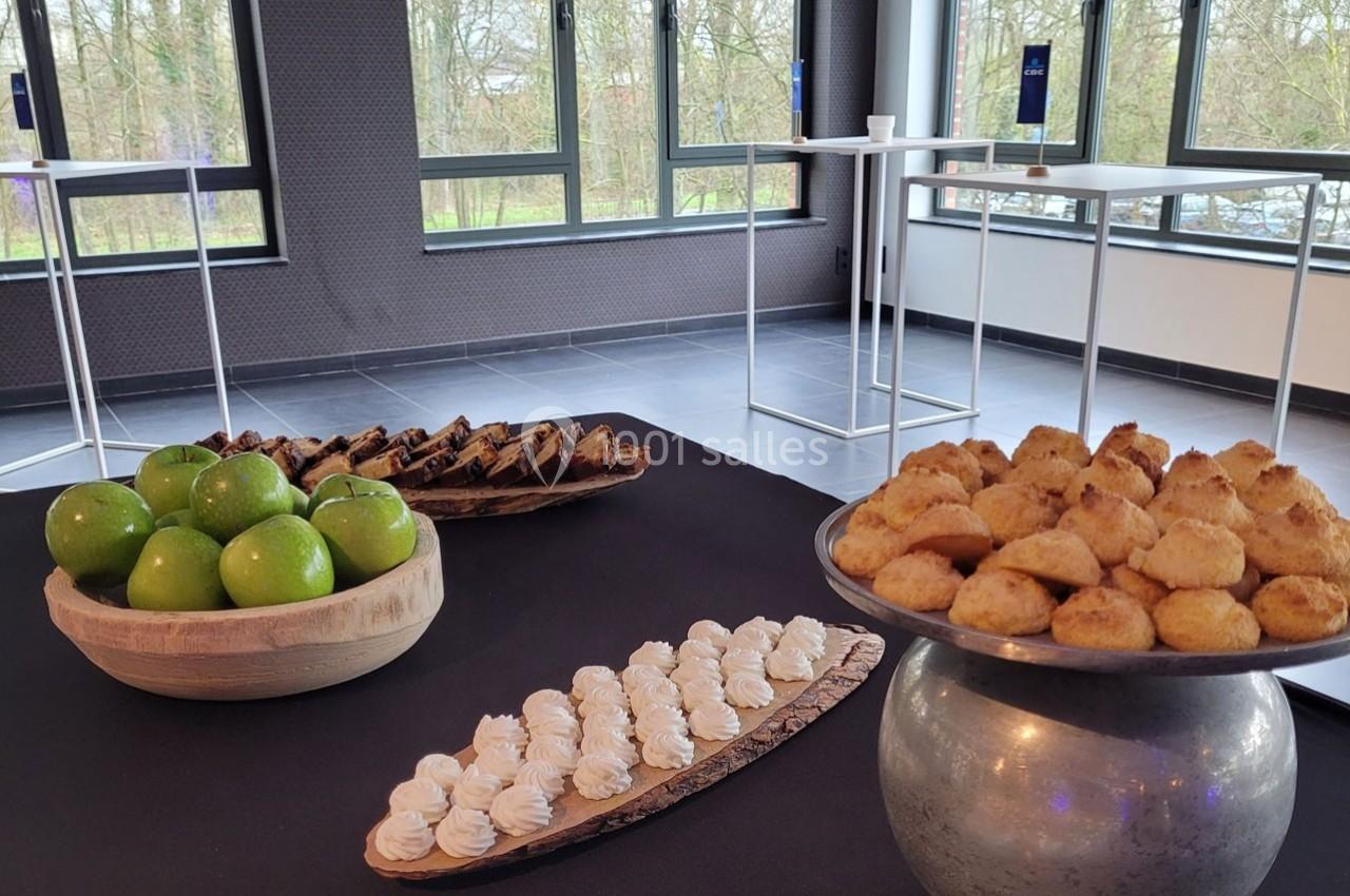 Plateau de desserts variés avec pommes vertes, meringues, biscuits et gâteaux dans une salle lumineuse.