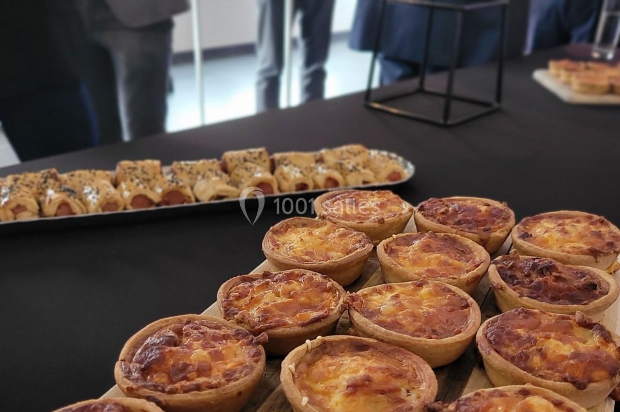 Plateau de mini-quiches au premier plan et assortiment de feuilletés en arrière-plan sur une table noire.