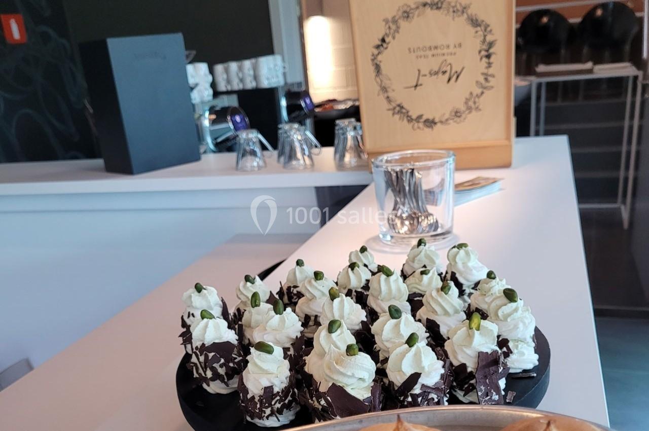 Plateau de desserts individuels garnis de crème chantilly et décorés de pistaches, posé sur un comptoir moderne.