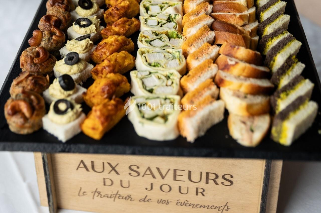 Plateau de canapés variés comprenant des bouchées salées, roulés et mini-sandwichs présentés sur un support en bois.