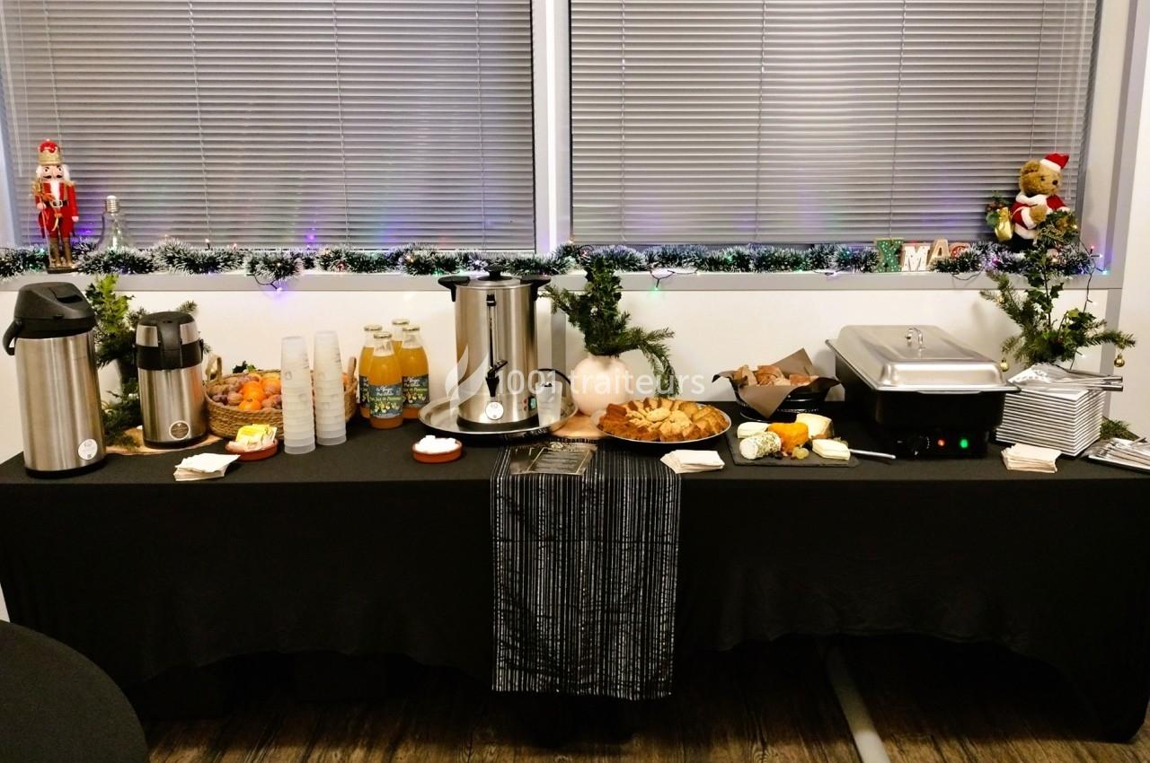 Table de buffet avec boissons chaudes, jus, viennoiseries, fruits et décorations festives.