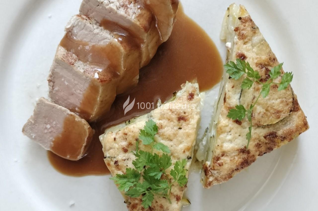 Assiette contenant un filet de viande nappé de sauce brune et deux parts de gratin garnies de feuilles de persil.