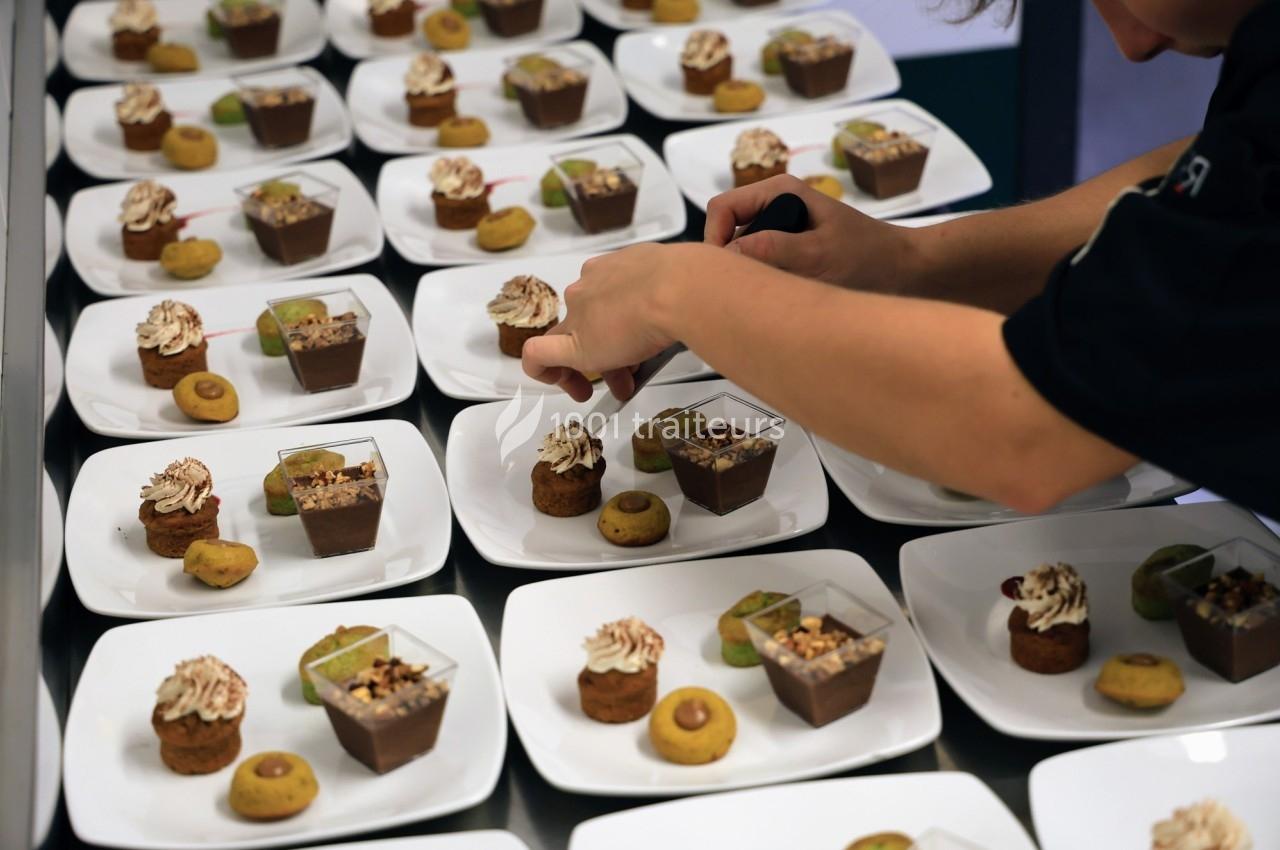 Un chef prépare des assiettes de desserts variés, disposées en rangées sur une table.