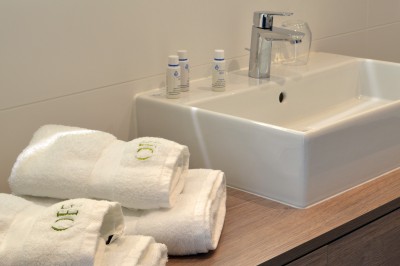 Lavabo moderne avec robinet chromé, serviettes blanches pliées et produits de toilette sur un plan en bois.