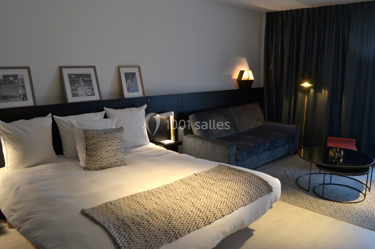 Chambre moderne avec lit double, canapé, table basse, éclairage tamisé et décorations murales encadrées.