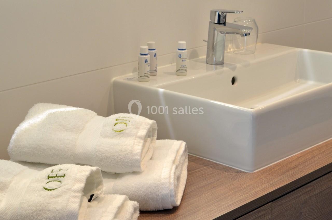 Lavabo moderne avec robinet chromé, serviettes blanches pliées et produits de toilette disposés sur un plan en bois.