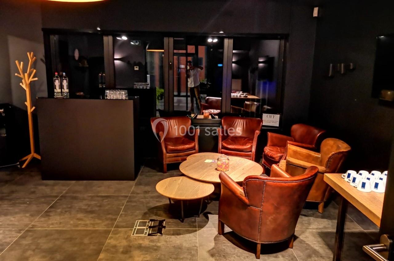 Espace lounge avec fauteuils en cuir, tables basses en bois et éclairage tamisé dans une ambiance moderne.