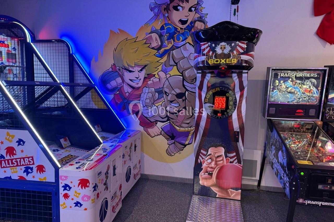 Jeu de boxe arcade entouré de bornes d'arcade et d'un flipper, avec une fresque murale de personnages animés.