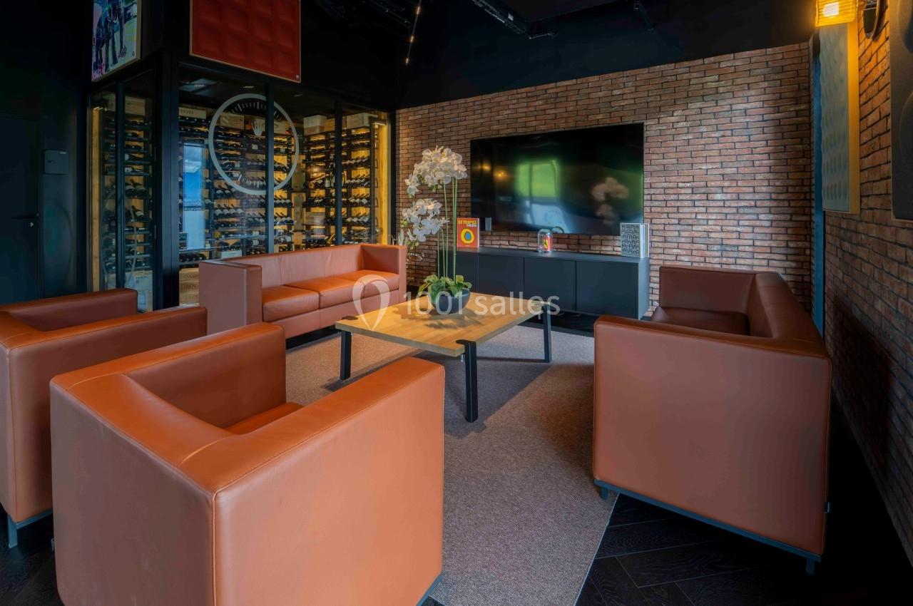 Salon moderne avec canapés en cuir orange, table basse en bois, mur en briques et écran mural.