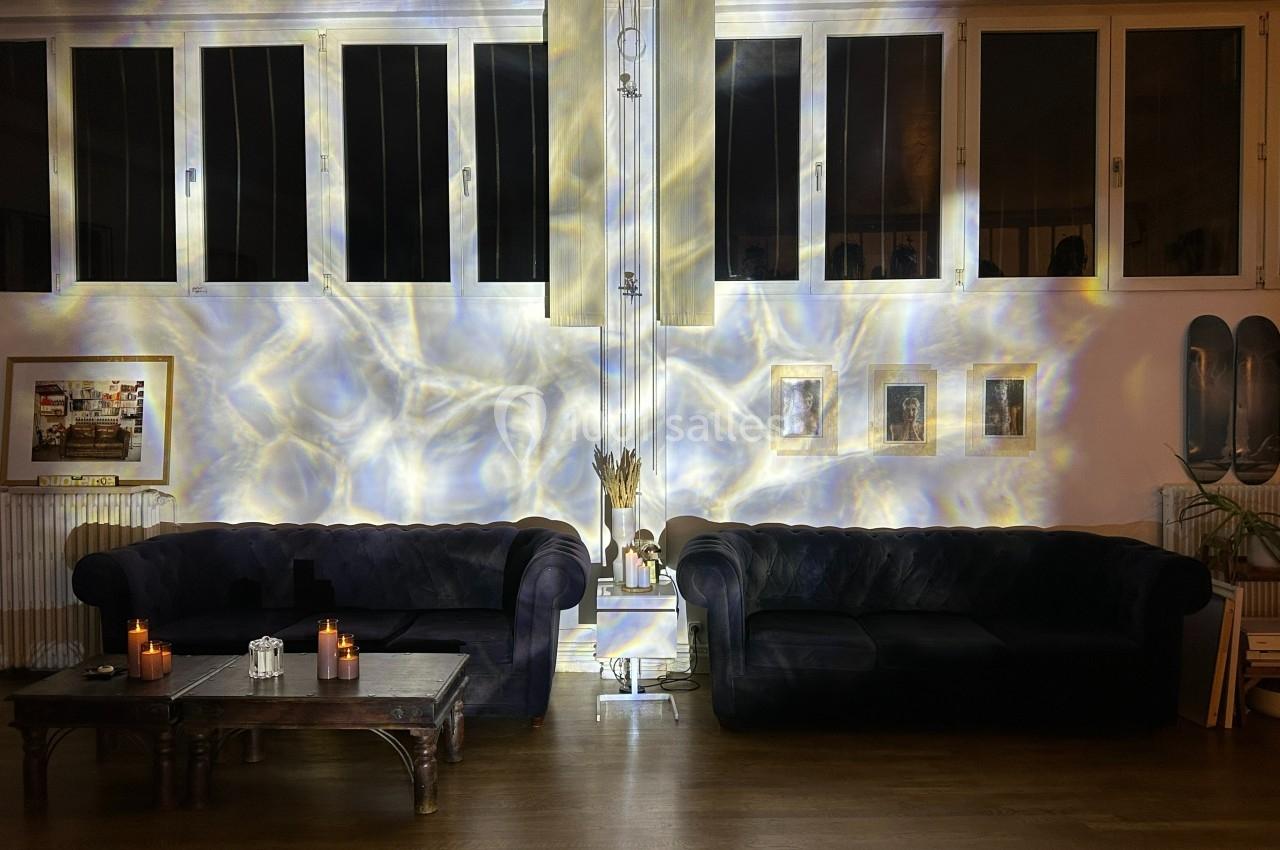 Deux canapés sombres entourent une table basse avec des bougies allumées, éclairés par des reflets lumineux sur les murs.