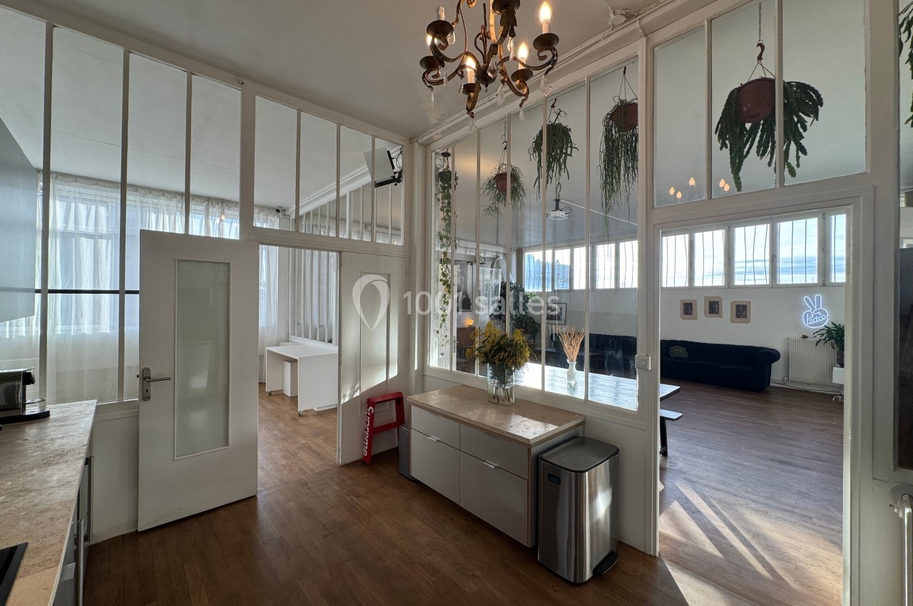Espace intérieur lumineux avec parquet, verrières, plantes suspendues et mobilier minimaliste.