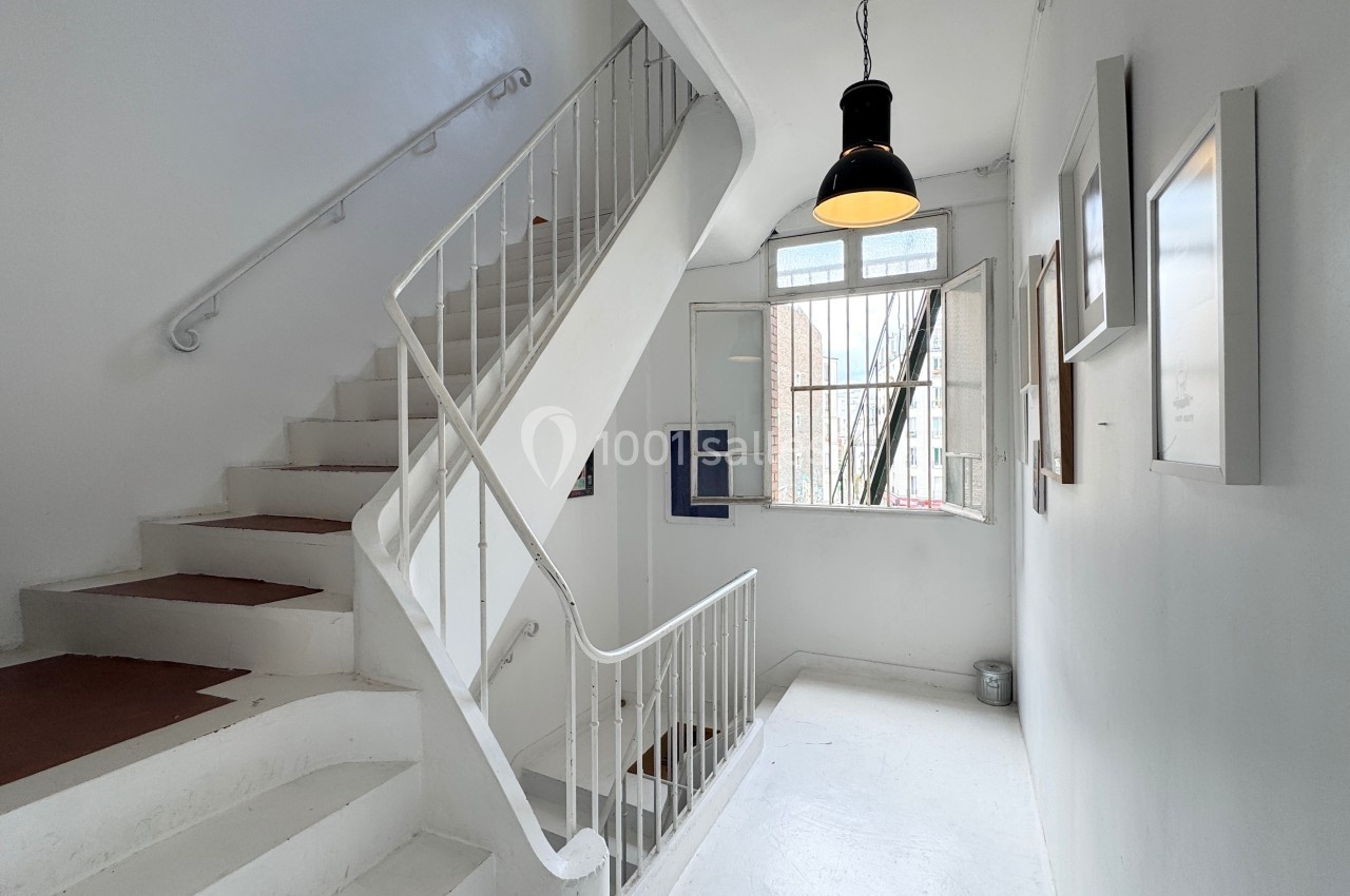 Escalier blanc dans un espace lumineux avec des cadres accrochés aux murs et une fenêtre ouverte.