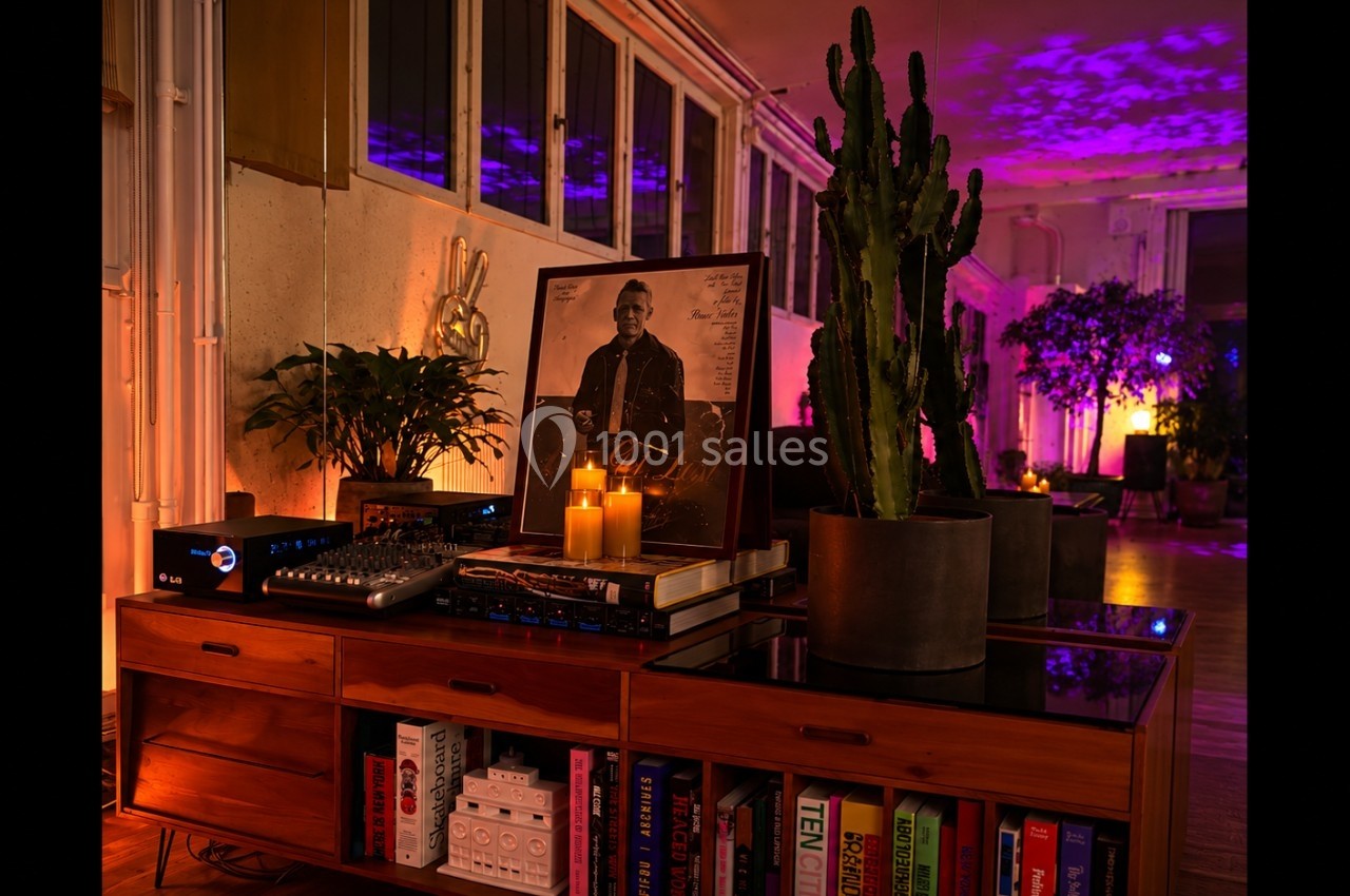 Meuble en bois avec livres, matériel audio, bougies allumées, photo encadrée et plantes dans une ambiance tamisée.