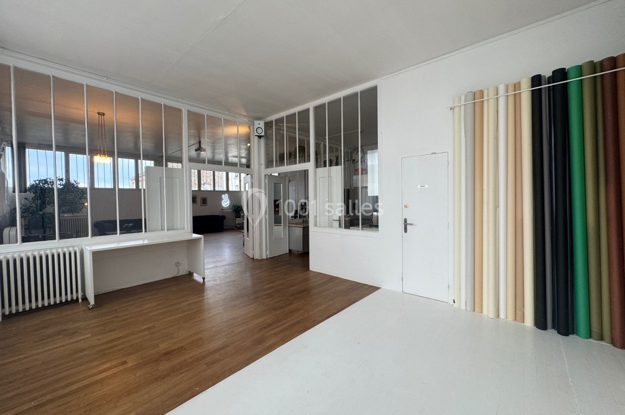 Espace intérieur lumineux avec parquet, murs blancs, cloisons vitrées et rideaux colorés à droite.