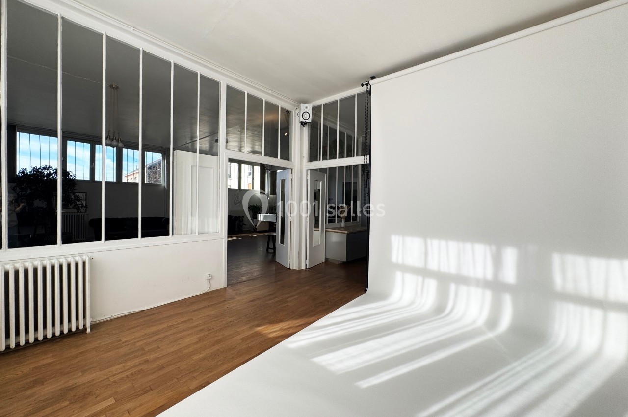 Studio lumineux avec parquet, mur blanc et grande verrière laissant entrer la lumière naturelle.
