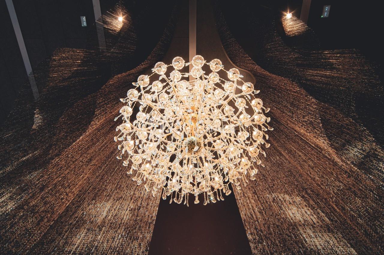 Lustre en cristal suspendu, éclairé, avec des rideaux sombres en arrière-plan.