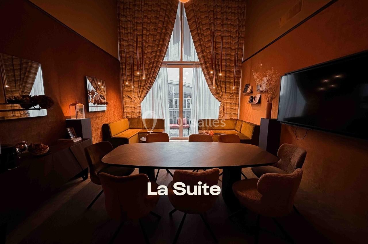 Salle de réunion chaleureuse avec table ovale, chaises rembourrées, banquettes et grande fenêtre donnant sur une terrasse.