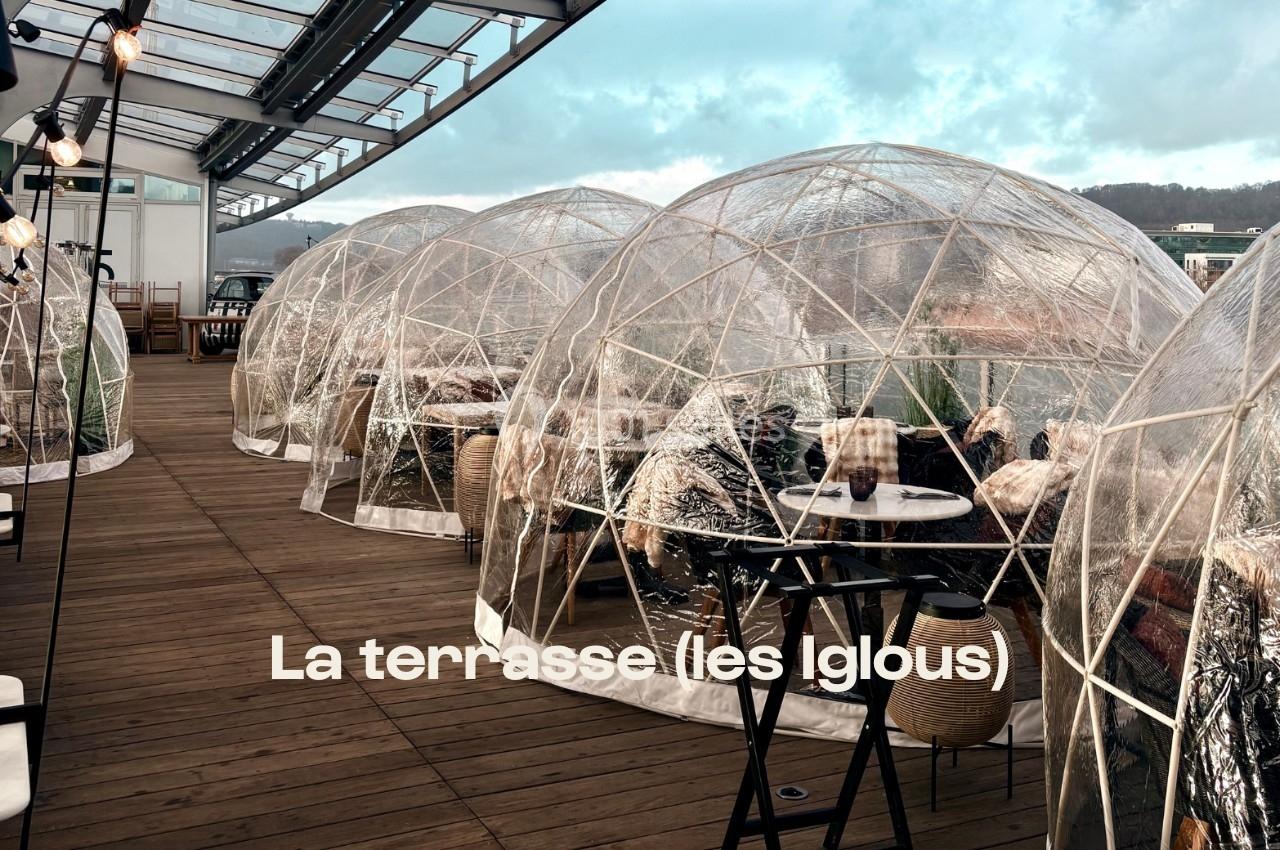 Terrasse en bois avec des igloos transparents aménagés pour des repas en extérieur, entourés d'un paysage naturel.
