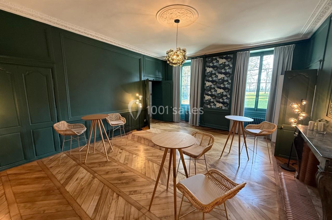 Salle lumineuse avec parquet en bois, murs verts, tables hautes et chaises en rotin, vue sur un jardin à travers les…