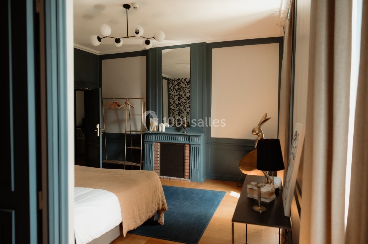 Chambre lumineuse avec lit double, cheminée décorative, portant à vêtements et mobilier moderne dans un style épuré.