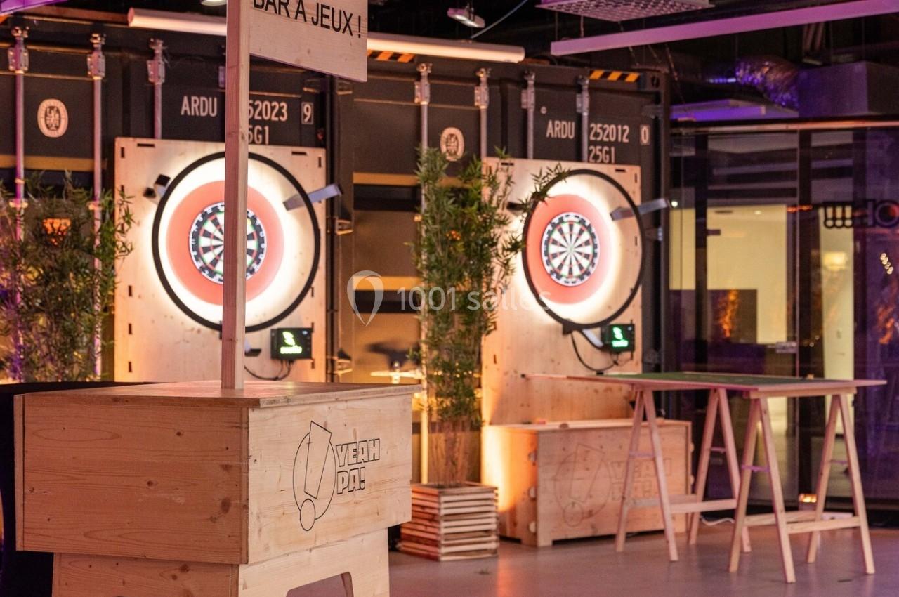 Espace intérieur avec cibles de fléchettes lumineuses, bar en bois et ambiance industrielle.