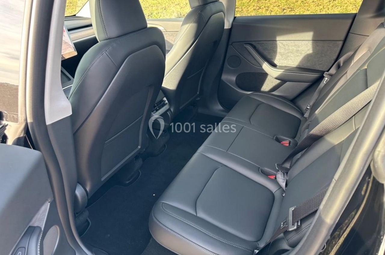 Sièges arrière d'une voiture avec revêtement en cuir noir, ceintures de sécurité et espace pour trois passagers.