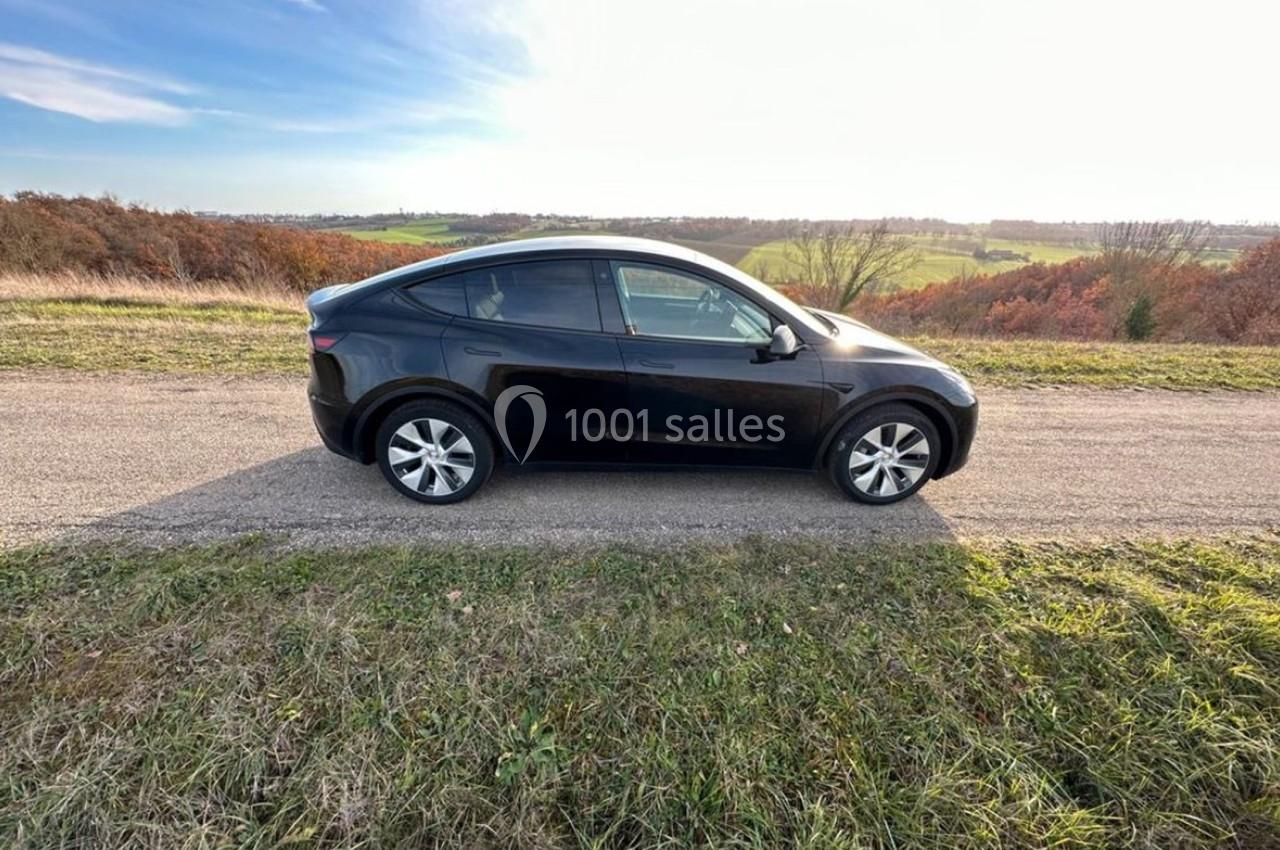 Voiture noire stationnée sur une route de campagne, entourée de champs et d'arbres sous un ciel dégagé.