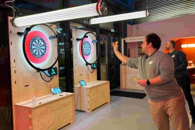 Des personnes jouent à un jeu de lancer de ballons de basket en plein air, entourées de spectateurs.