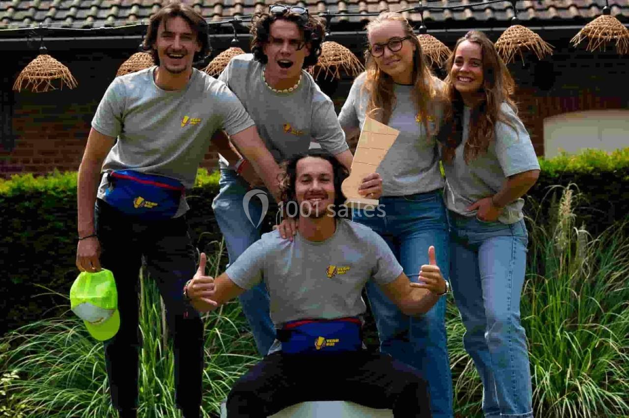 Un groupe de cinq personnes souriantes posant sur un podium dans un jardin devant un bâtiment en briques.