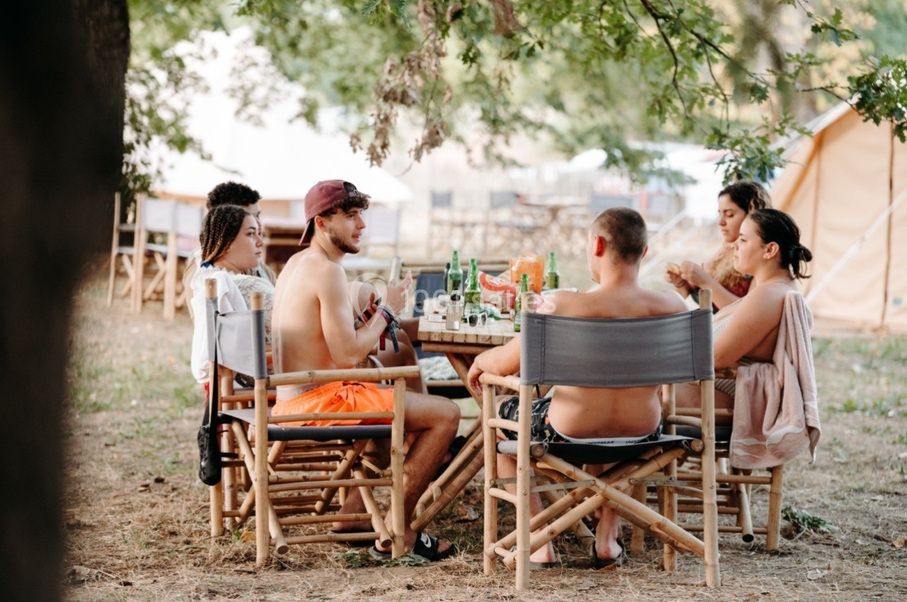 Un groupe de personnes assises autour d'une table en plein air, discutant et partageant un repas sous des arbres.