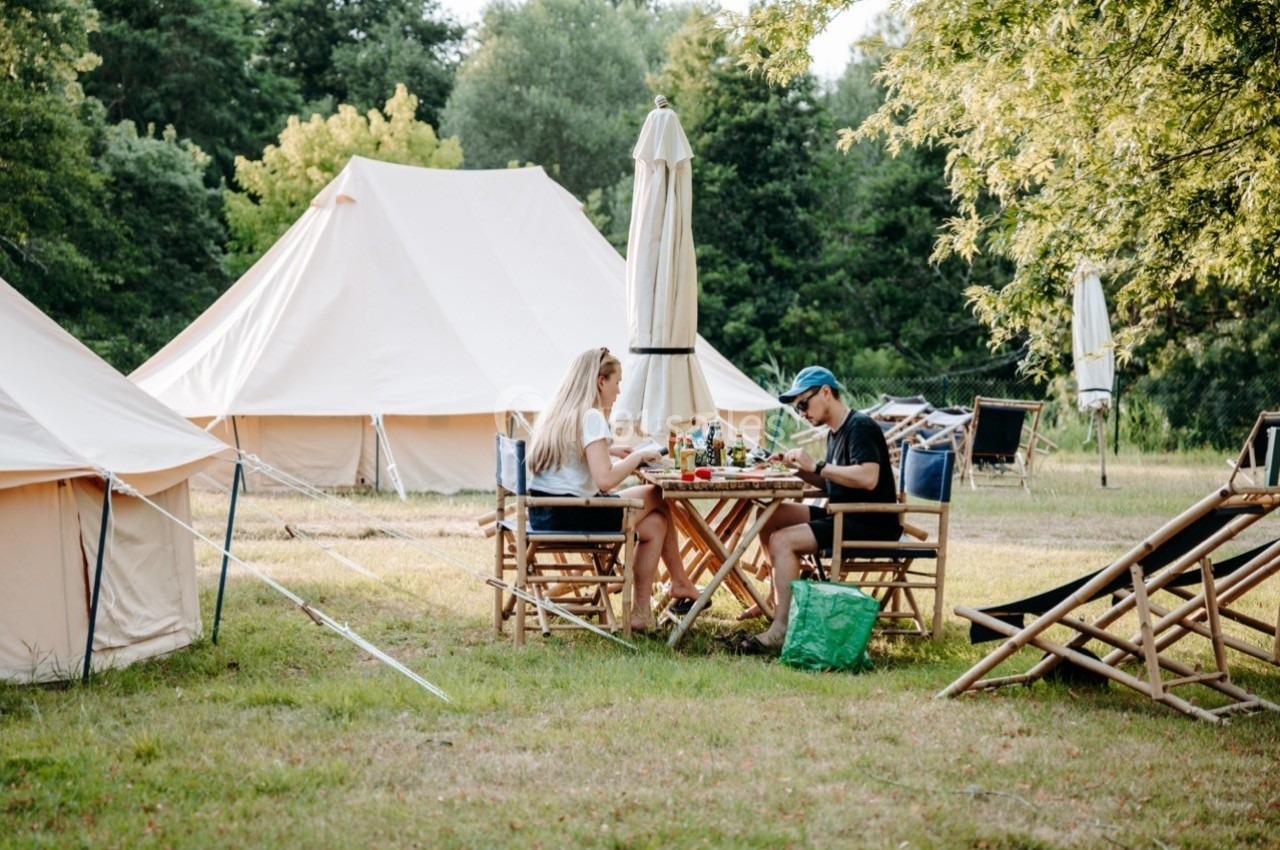 Deux personnes déjeunent à une table en bois devant des tentes dans un cadre verdoyant.