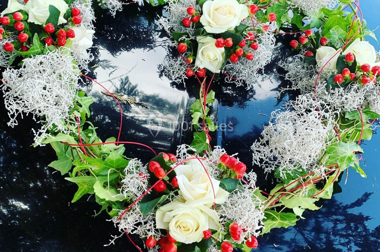 Décoration florale en forme de cœur avec roses blanches, baies rouges et feuillage, posée sur une surface noire brillante.