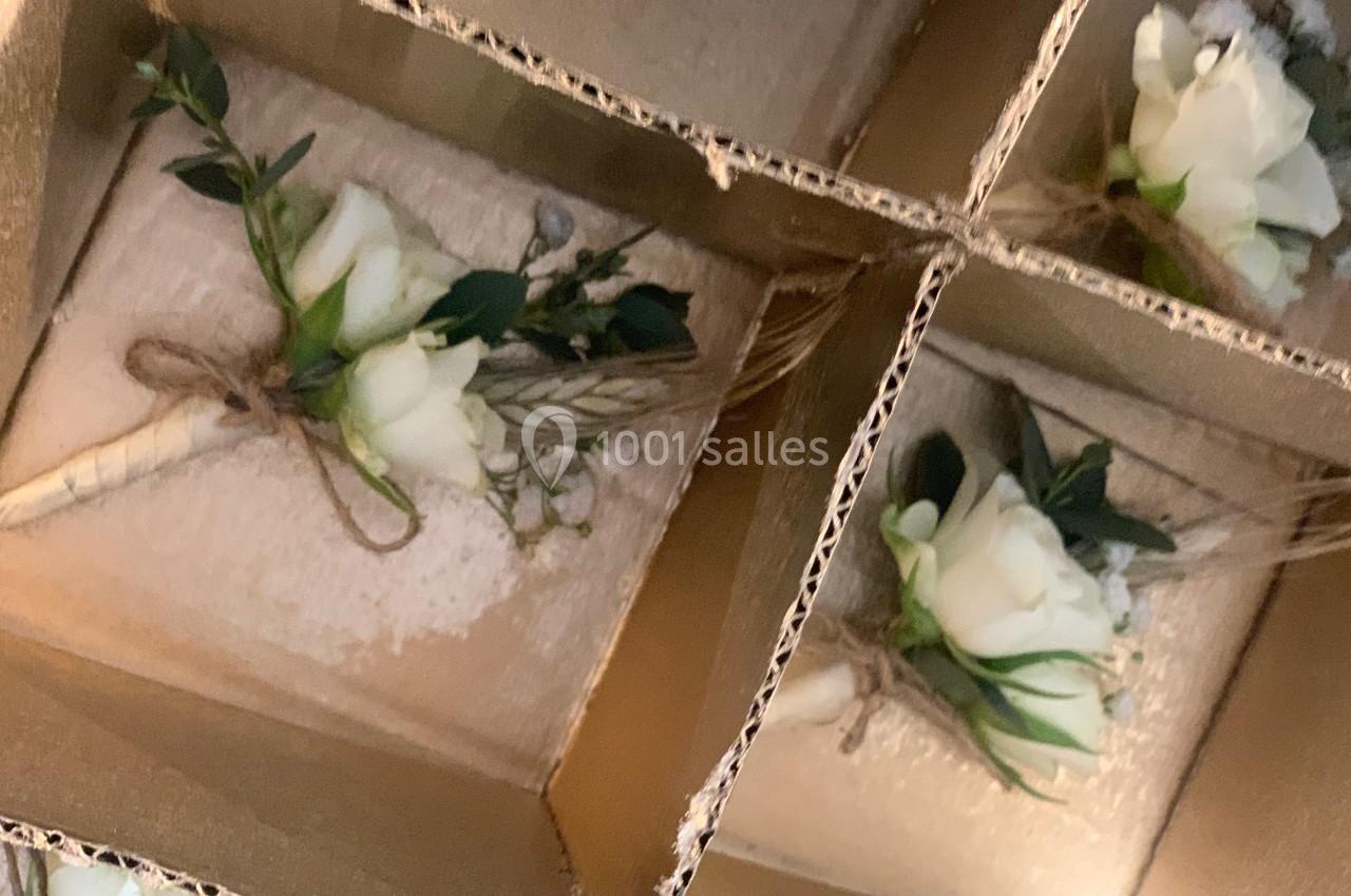 Boutonnières en fleurs blanches et feuillage vert, disposées dans des compartiments en carton.