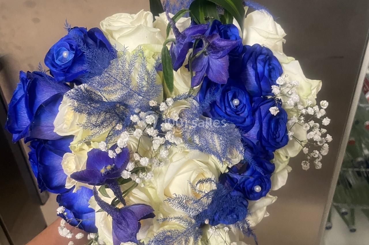 Bouquet de roses blanches et bleues avec des touches de gypsophile et de feuillage décoratif, tenu à la main.