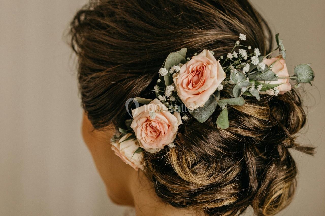 Chignon brun orné de roses roses et de petites fleurs blanches, vu de dos.