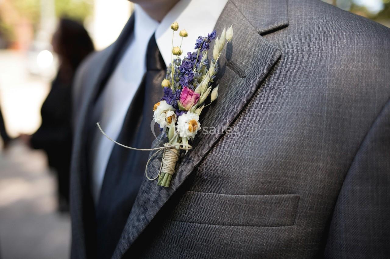 Boutonnière composée de fleurs sauvages colorées attachées avec une ficelle, portée sur un costume gris.