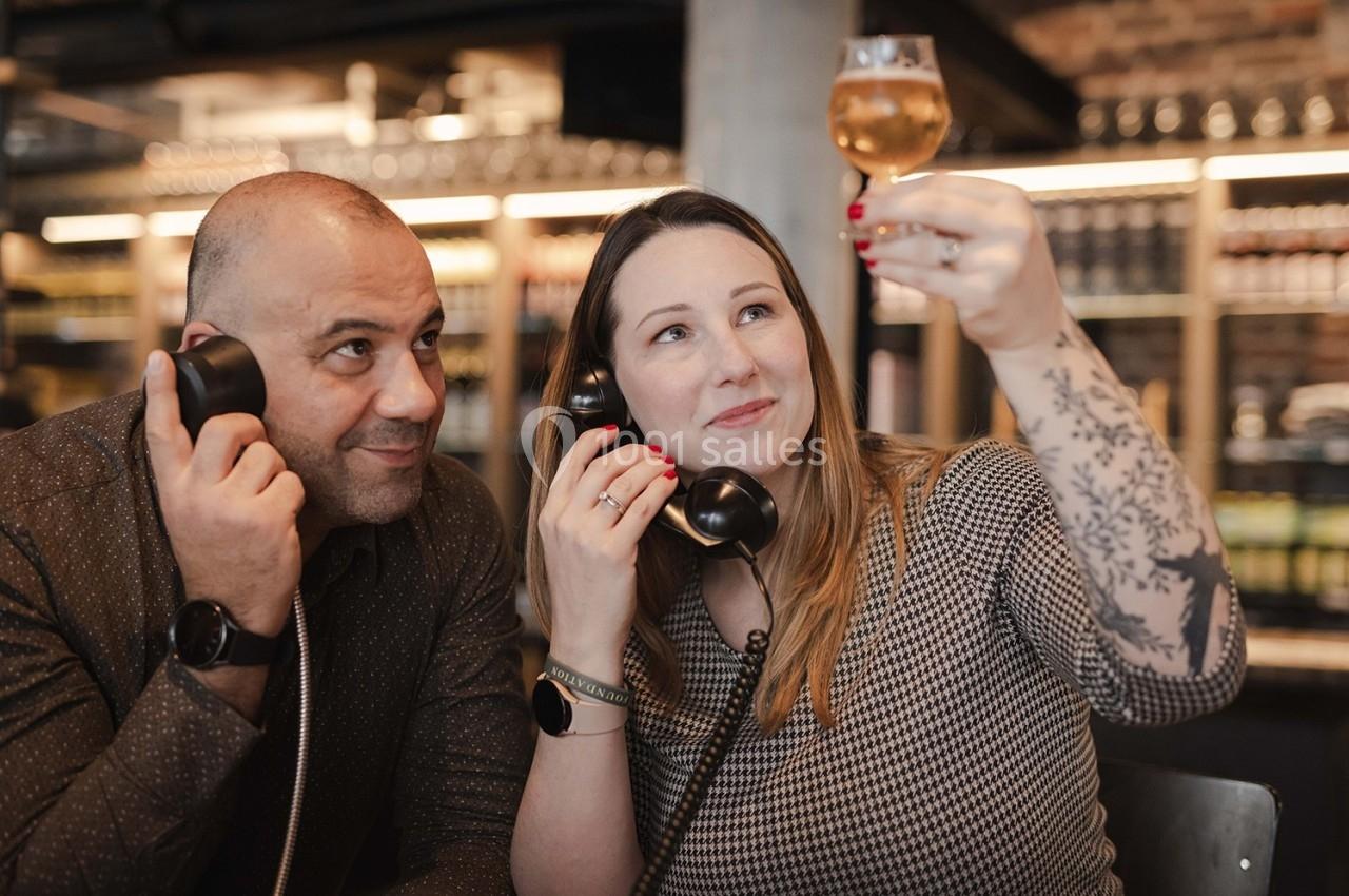 Dégustation Un homme et une femme tenant des combinés téléphoniques, la femme examine un verre de boisson dorée.