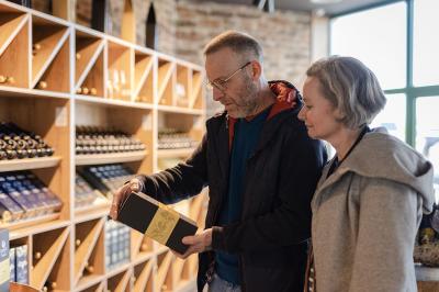 Miniature Magasin Terroir des Trolls Un homme et une femme regardent une boîte dans un magasin de vins avec des étagères remplies de bouteilles en arrière-plan.
