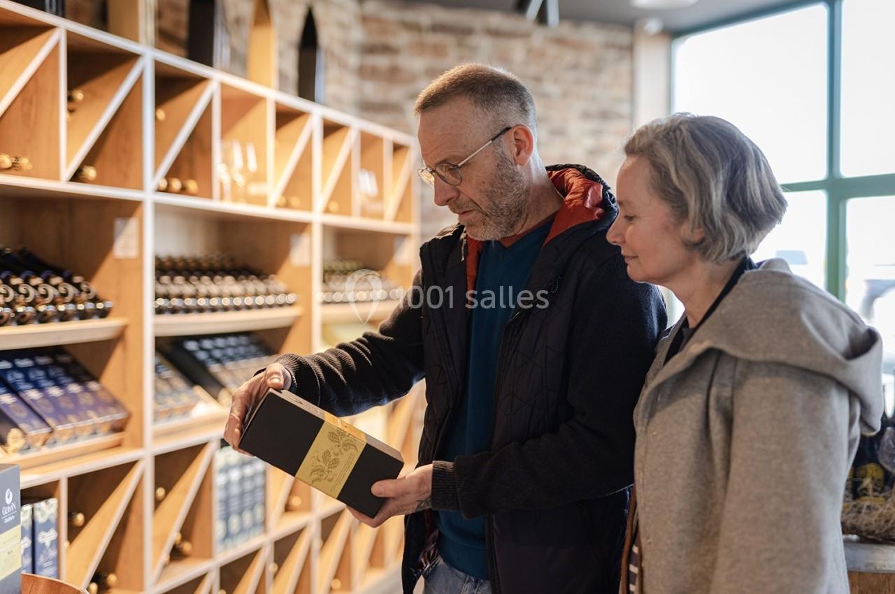Magasin Terroir des Trolls Un homme et une femme regardent une boîte dans un magasin de vins avec des étagères remplies de bouteilles en arrière-plan.
