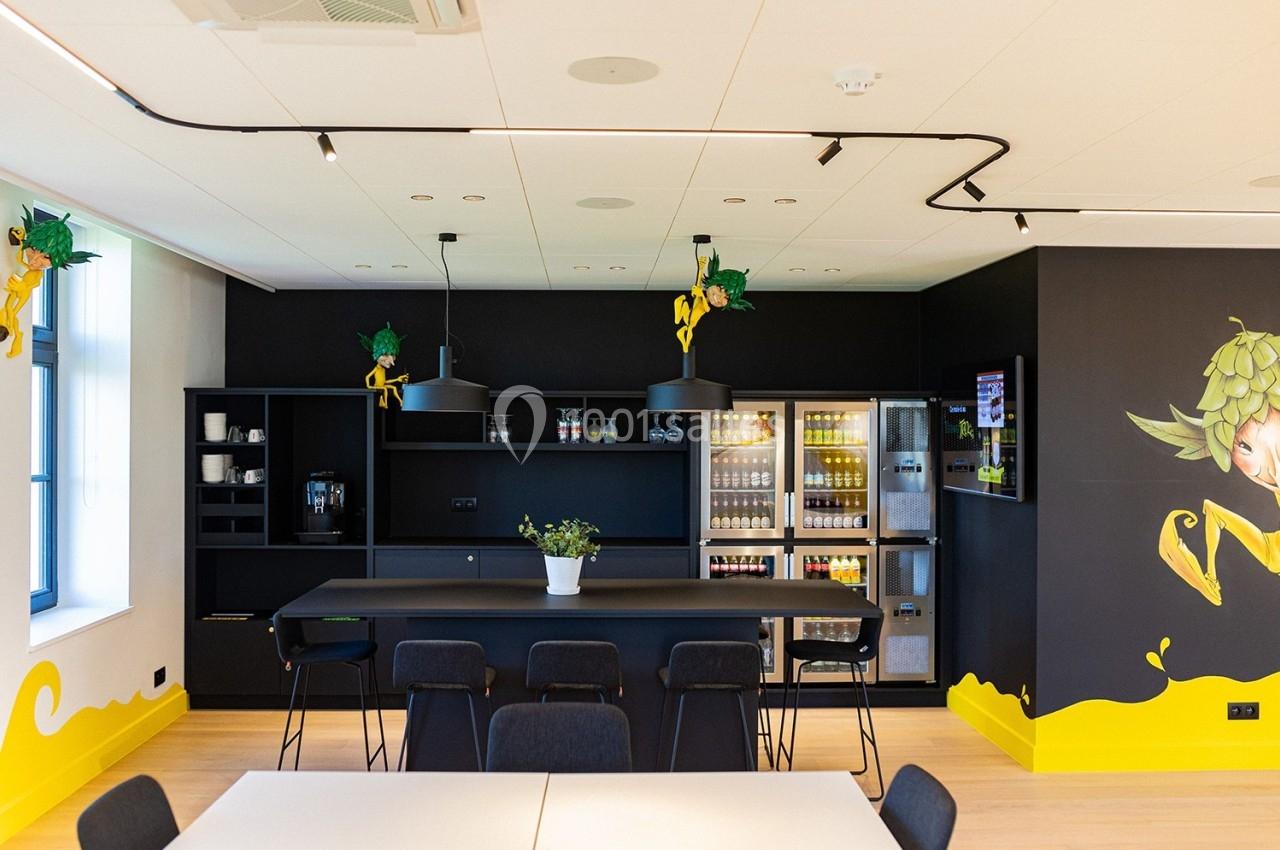 Salle Cuvée des Trolls Cuisine moderne avec comptoir noir, chaises, réfrigérateurs vitrés, machines à café et décoration murale colorée.