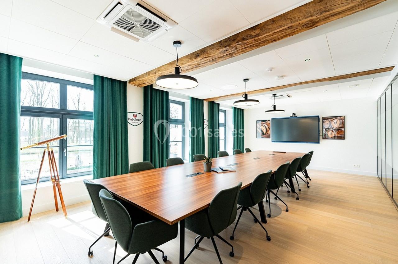 Salle Dubuisson Salle de réunion lumineuse avec grande table en bois, chaises noires, écran mural et fenêtres donnant sur l'extérieur.