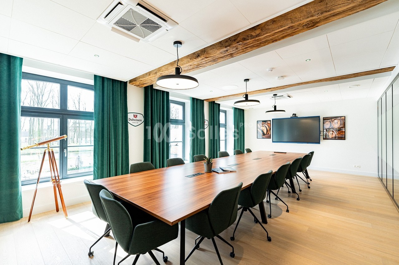 Salle de réunion lumineuse avec grande table en bois, chaises noires, écran mural et fenêtres donnant sur l'extérieur.