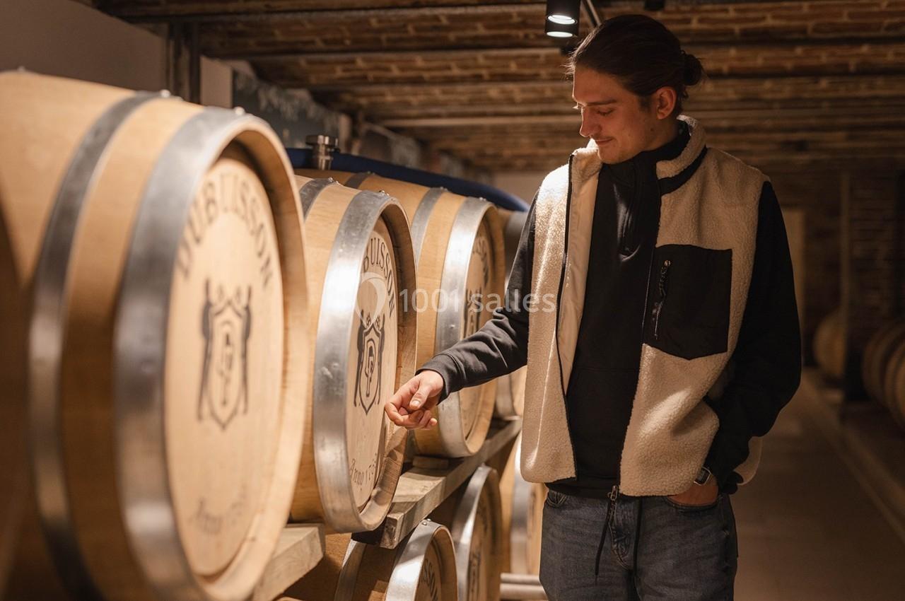 Visite de la Brasserie Un homme observe attentivement des fûts en bois alignés dans une cave voûtée.
