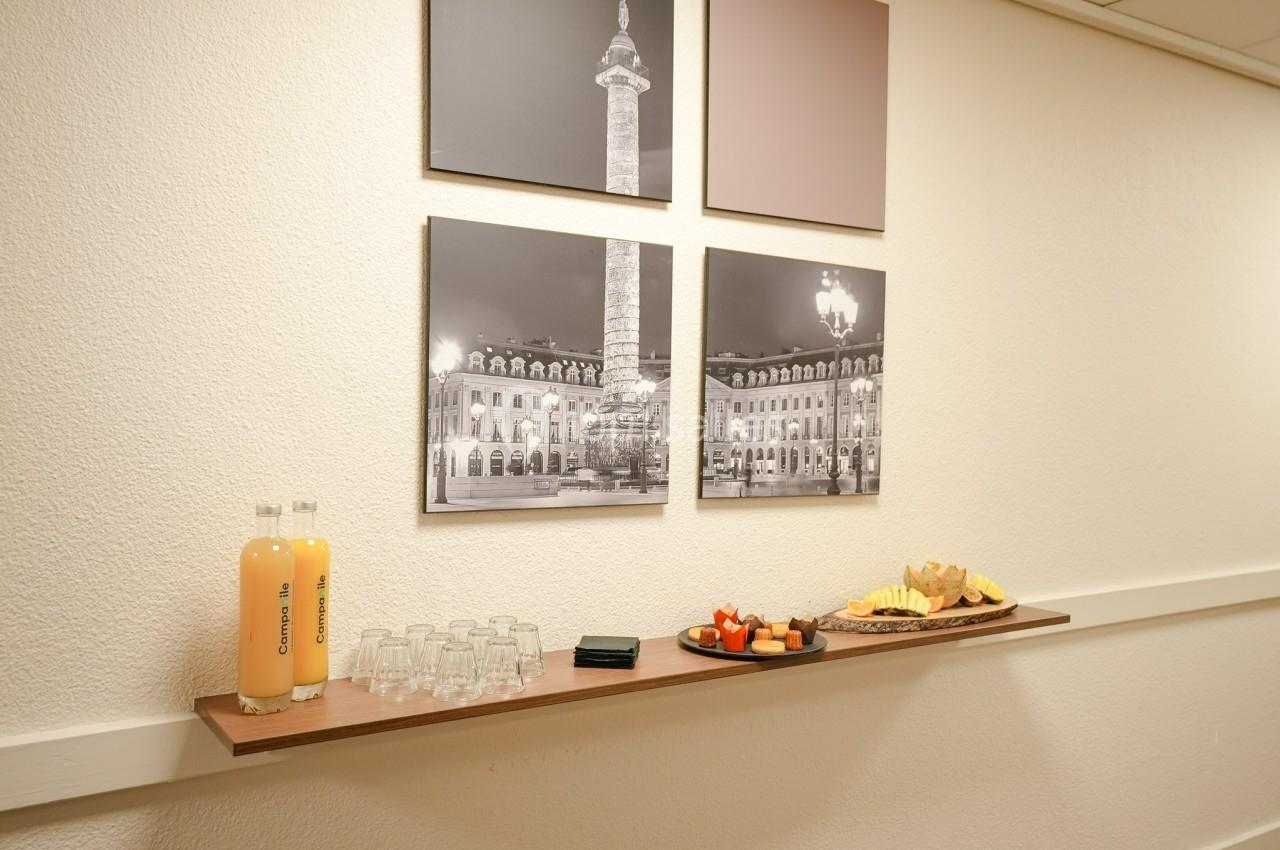 Plateau avec jus d'orange, verres, fruits et viennoiseries sur une étagère, devant des photos en noir et blanc.