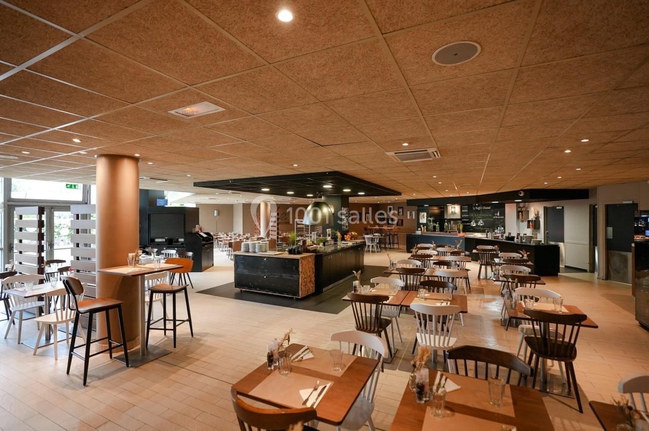 Salle de restaurant spacieuse avec tables en bois, chaises assorties et buffet central sous un éclairage chaleureux.
