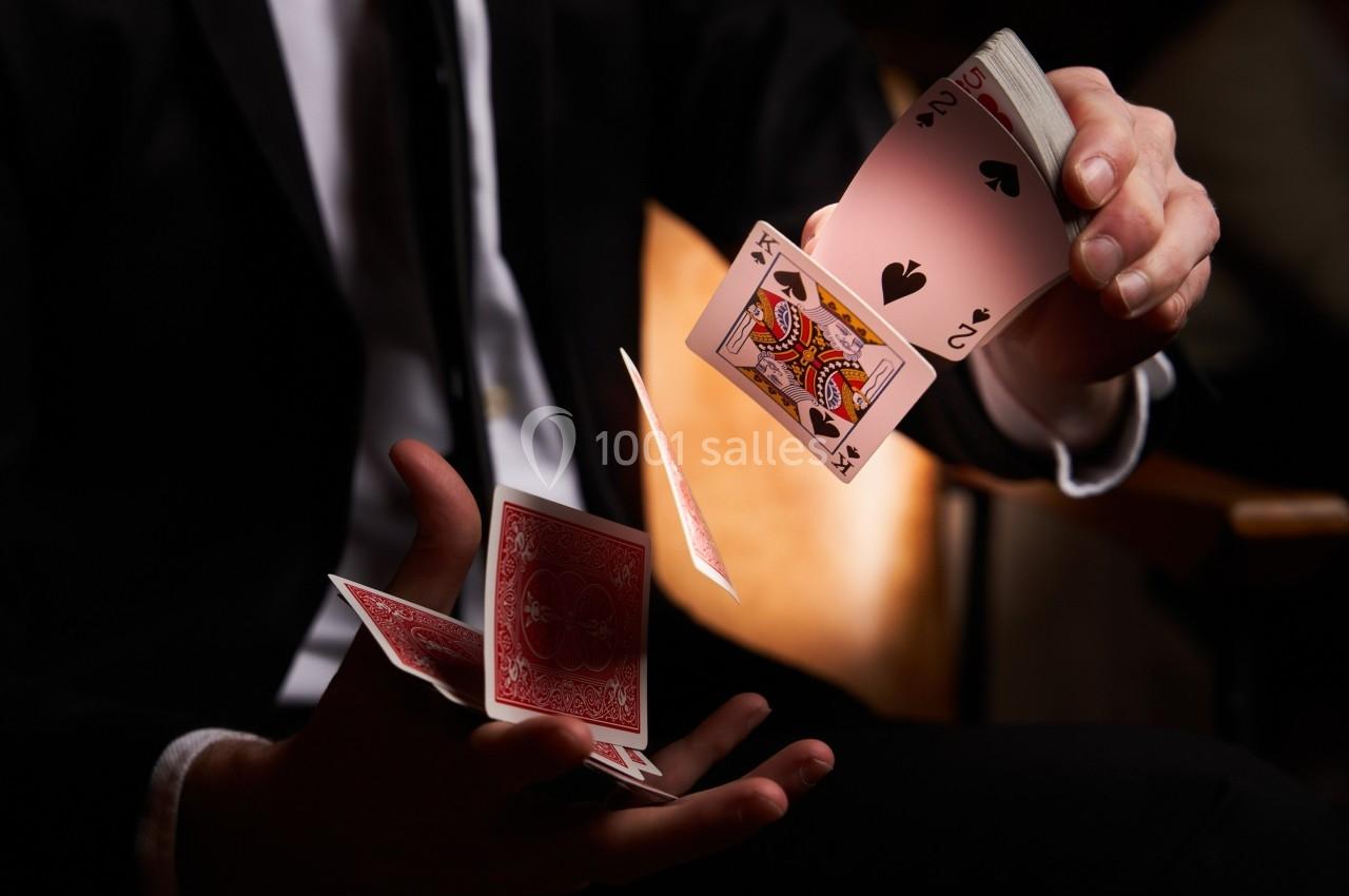 Un magicien en costume réalise un tour de cartes en les faisant flotter entre ses mains.